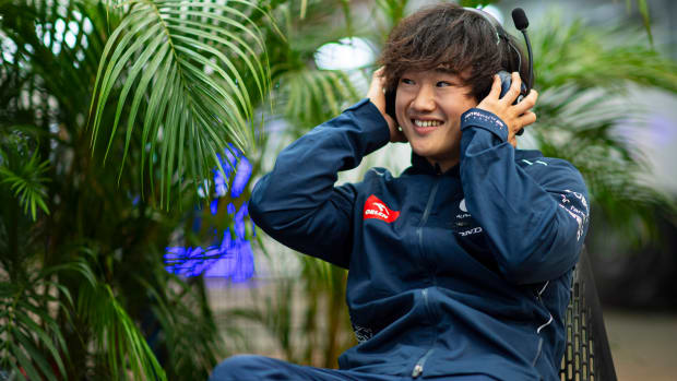 AlphaTauri driver Yuki Tsunoda smiles during an interview while wearing a headset.